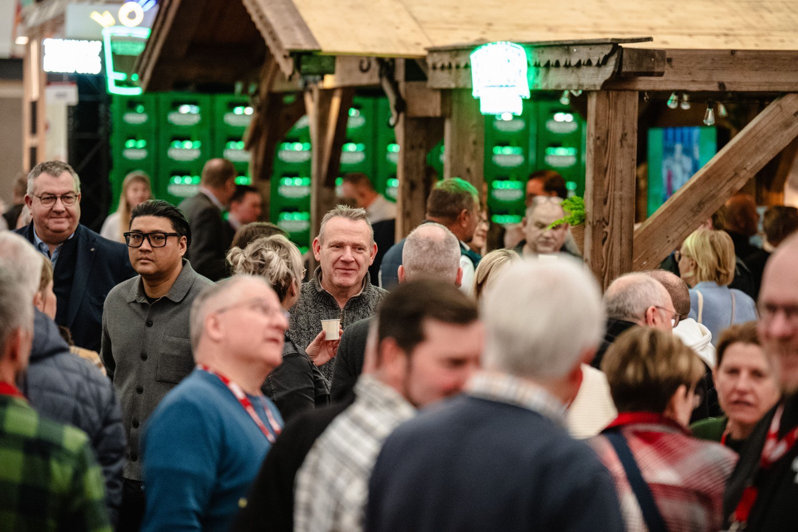 Menschenmenge in einer Halle mit Holzbauten und gr&uuml;nen Leuchten im Hintergrund