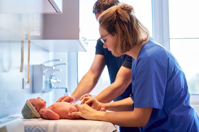 Zwei Menschen in blauen Oberteilen wickeln ein Baby.