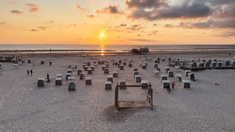 Ein weißer Sandstrand, auf dem Strandkörbe stehen. Die Sonne steht sehr tief.