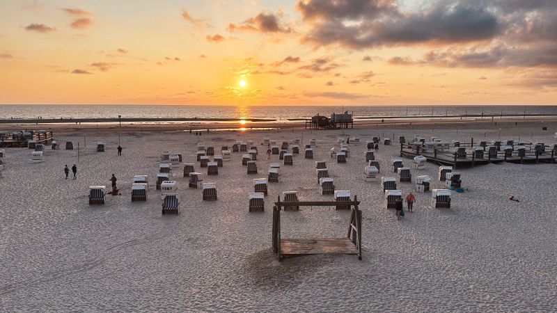 Ein weißer Sandstrand, auf dem Strandkörbe stehen. Die Sonne steht sehr tief.
