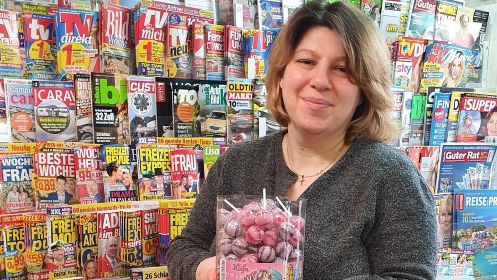 Eine Frau steht vor einem Zeitschriftenregal. In ihrer Hand hält sie eine Lolli-Packung.