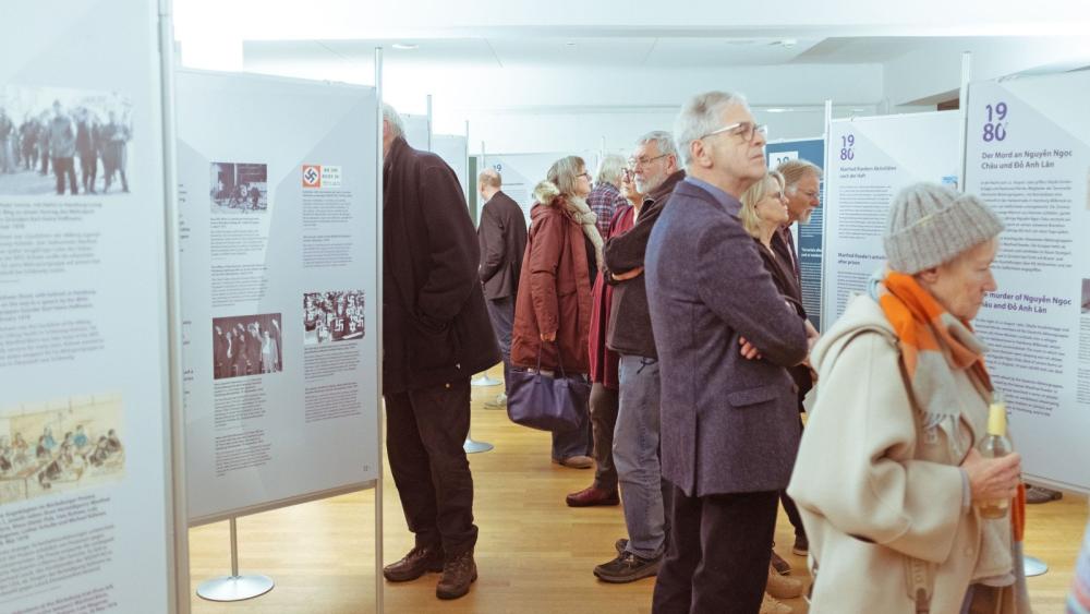 Mehrere Personen betrachten Ausstellungstafeln in einem hellen Raum mit Holzboden.