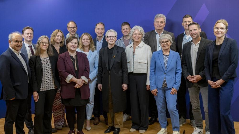 Menschen stehen auf hellem Parkett vor einer blauen Wand.