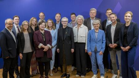 Menschen stehen auf hellem Parkett vor einer blauen Wand.