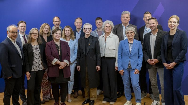 Menschen stehen auf hellem Parkett vor einer blauen Wand.