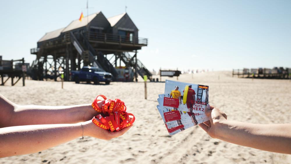 Rotes Armband in St Peter-Ording am Strand. Im Hintergrund ein Pfahlbau.
