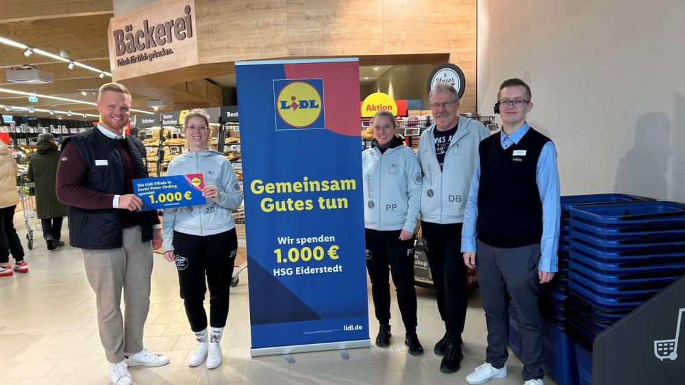 Fünf Personen stehen in einem Supermarkt vor einem Aufsteller mit dem Lidl-Logo und dem Text 'Gemeinsam Gutes tun Wir spenden 1.000 € HSG Eiderstedt', zwei Personen halten einen Scheck mit '1.000 €'