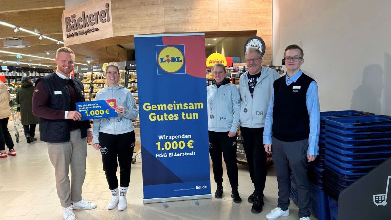 Fünf Personen stehen in einem Supermarkt vor einem Aufsteller mit dem Lidl-Logo und dem Text 'Gemeinsam Gutes tun Wir spenden 1.000 € HSG Eiderstedt', zwei Personen halten einen Scheck mit '1.000 €'