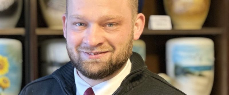 Ein Mann lächelt. Im Hintegrund Urnen.
