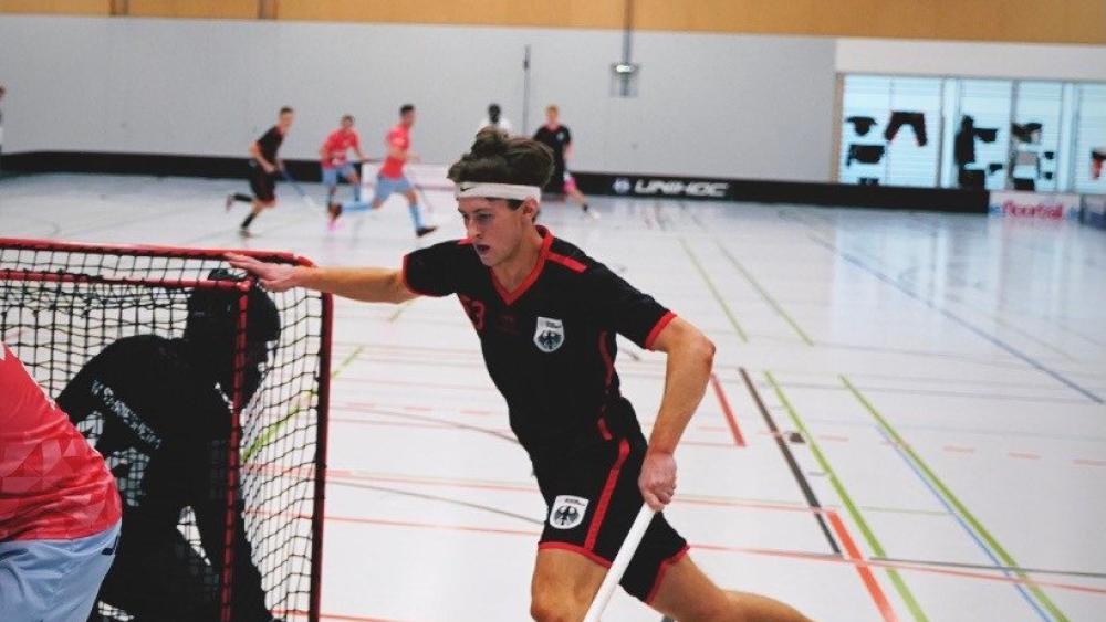 Ein Junge läuft in einer Sporthalle hinter ein Floorballtor und guckt auf jemanden, der nicht zu erkennen ist.