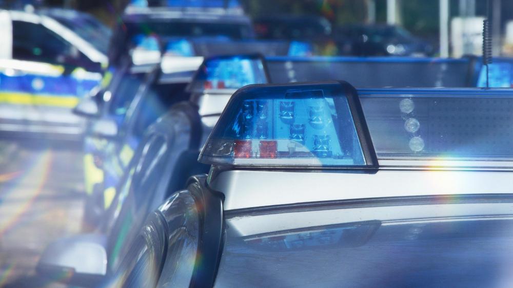 Mehrere hintereinander geparkte Polizeiautos mit blauen Blaulichtern auf den Dächern.