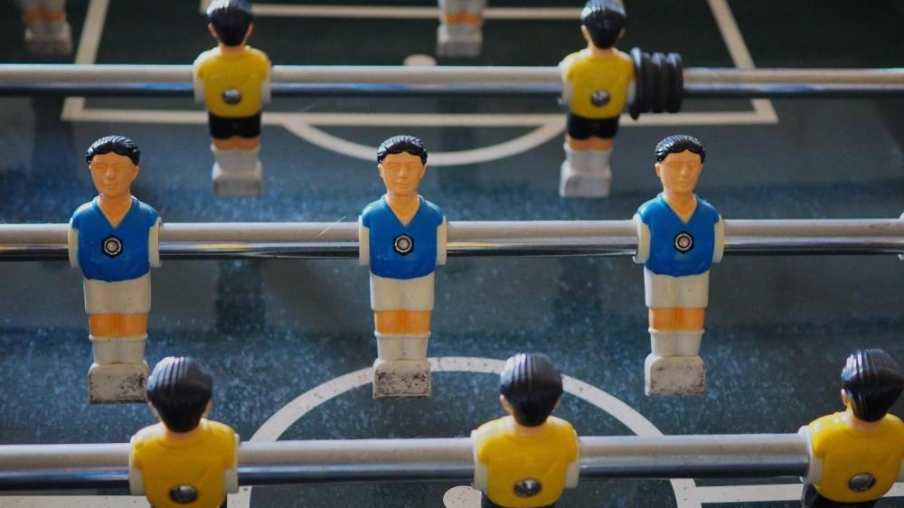 Tischfußballfiguren in blauen und gelben Trikots auf Metallstangen.