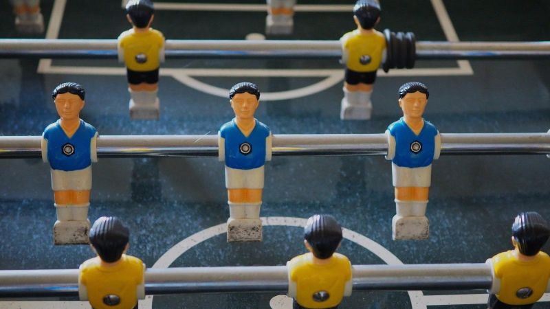 Tischfußballfiguren in blauen und gelben Trikots auf Metallstangen.