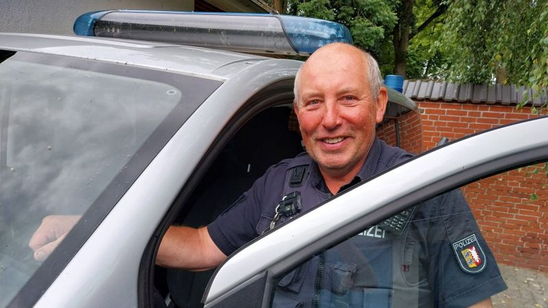 Ein Polizist steht lädcheln an der geöffneten Fahrertür eines Polizeiautos