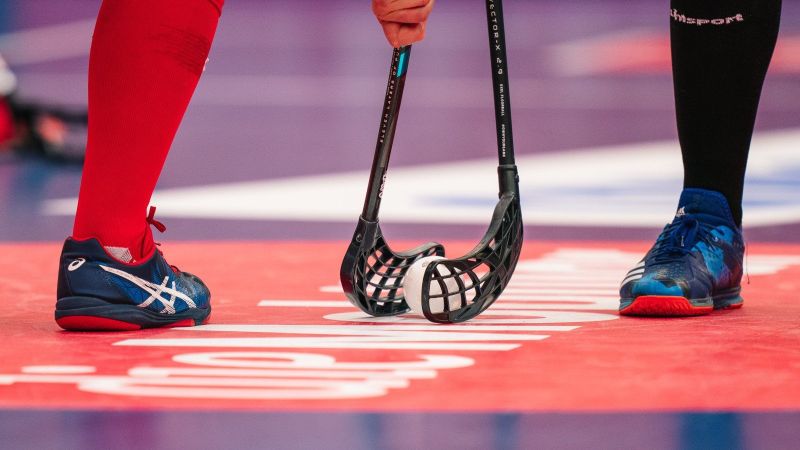 Floorballschläger gegenüber, dazwischen ein Floorball (Lochball aus Plastik in Apfelgröße).