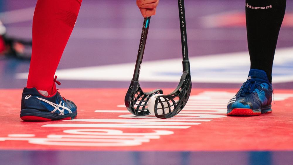 Floorballschläger gegenüber, dazwischen ein Floorball (Lochball aus Plastik in Apfelgröße).