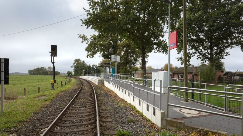 Blick auf den Bahnsteig, die Gleise und den Bahnsteigzugang mit dem Wetterschutzhäuschen, einem neuen Dynamischen Schriften Anzeiger (DSA+), einer neuen Uhr und dem Fahrkartenautomat am Bahnhof Süderdeich nach der Aufwertung im Rahmen des Konzepts Zukunftsbahnhof (ZKB) durch verschiedene bauliche und gestalterische Maßnahmen.