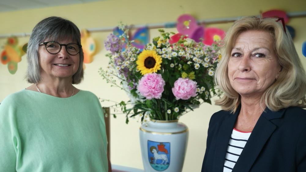 Zwei Frauen in einem gelben Raum. Zwischen ihnen eine Blumenvase, auf der das Wappen der Stadt Garding abgebildet ist.