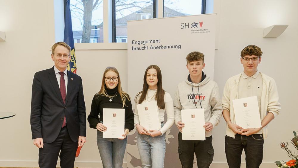 Ministerpräsident und junge Retter mit Urkunden in einem hellen Raum.