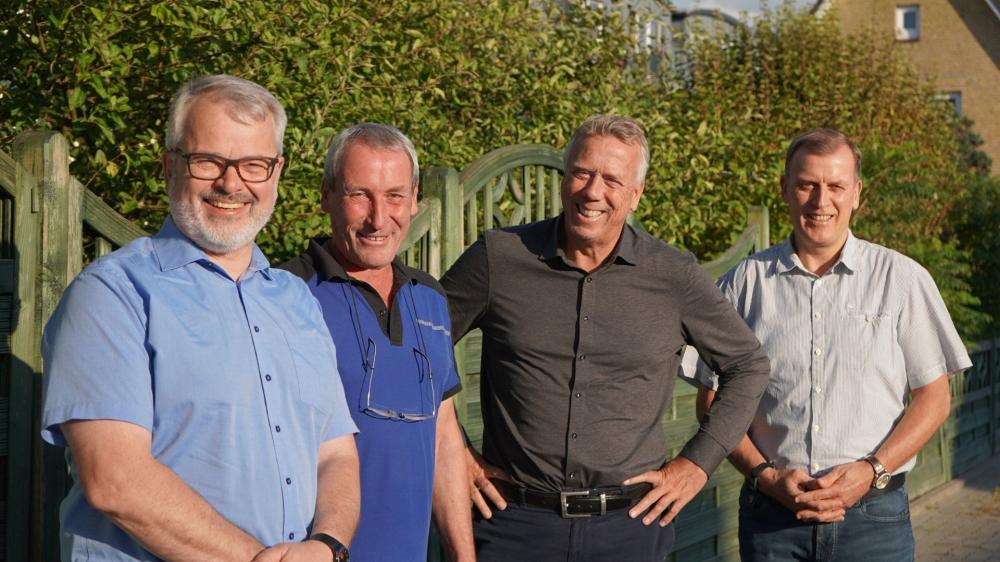 Vier Männer vor einem grünen Holz-Gartenzaun.