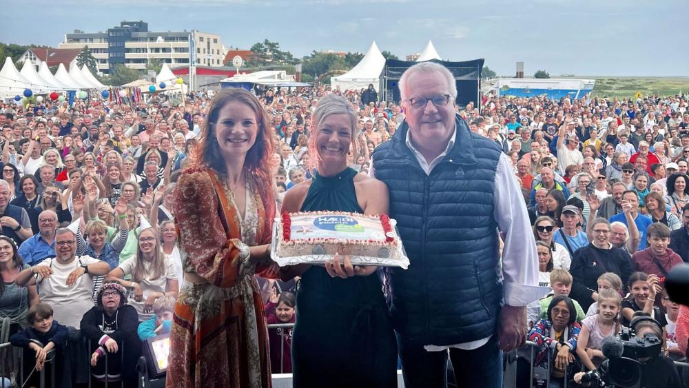 Drei Personen stehen auf einer Bühne in St. Peter-Ording. Im Hintergrund viele Menschen.