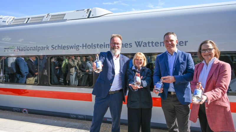 Vier Personen vor einem ICE-L der Deutschen Bahn. Auf dem Zug in grau 