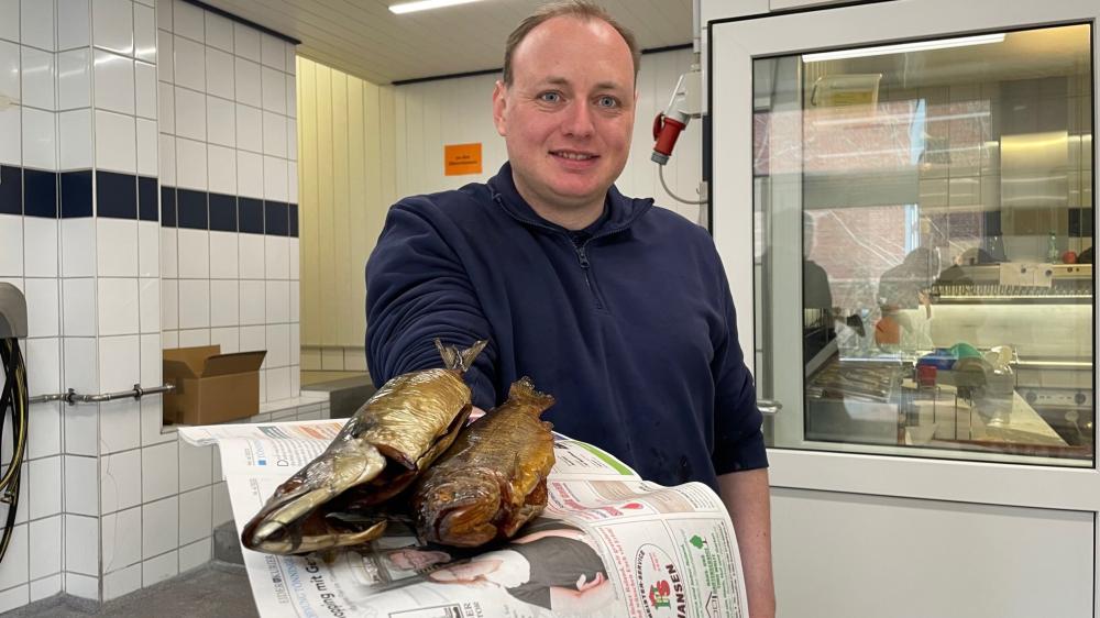 Ein Mann hält zwei Fische eingewickelt in den Eider-Kurier.