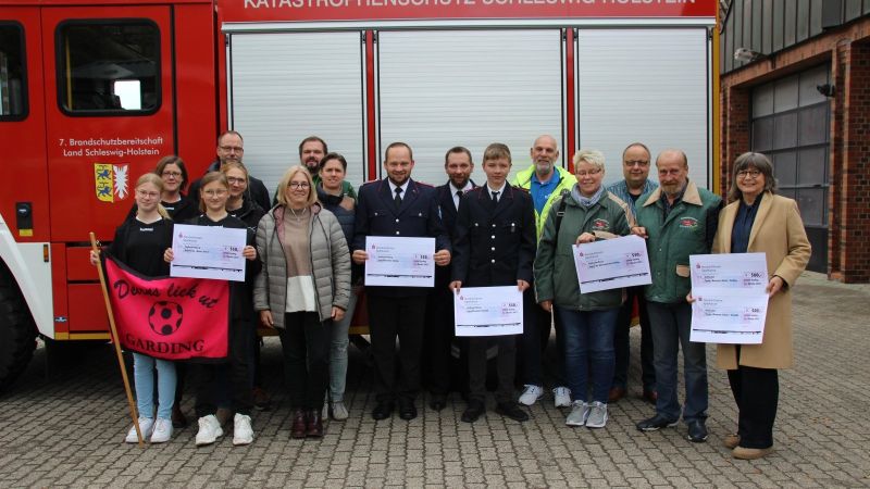 Eine Gruppe von Menschen steht vor einem Feuerwehrauto. Auf dem Auto steht 