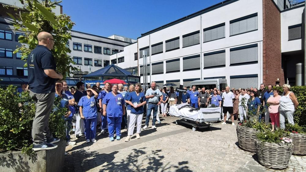 Menschen stehen versammelt vor einem Eingang eines Krankenhauses.