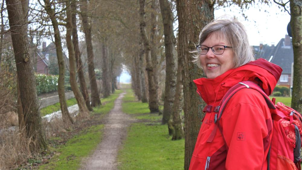 Eine Frau in dorter Funktionsjacke blickt lächelnd über die Schulter ins Bild.