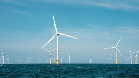 Weiße Windkraftanlagen in blauem Meer. Im Hintergrund hellblauer Himmel.