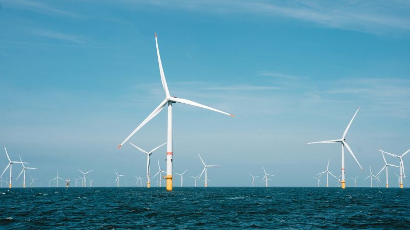 Weiße Windkraftanlagen in blauem Meer. Im Hintergrund hellblauer Himmel.