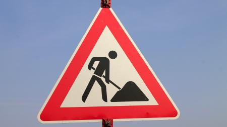 Verkehrsschild mit rotem Dreieck und schwarzer Piktogrammfigur, die mit Schaufel arbeitet.