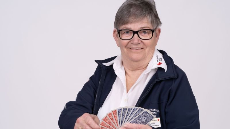 Frau vor weißem Hintergrund mit Spielkarten in der Hand.
