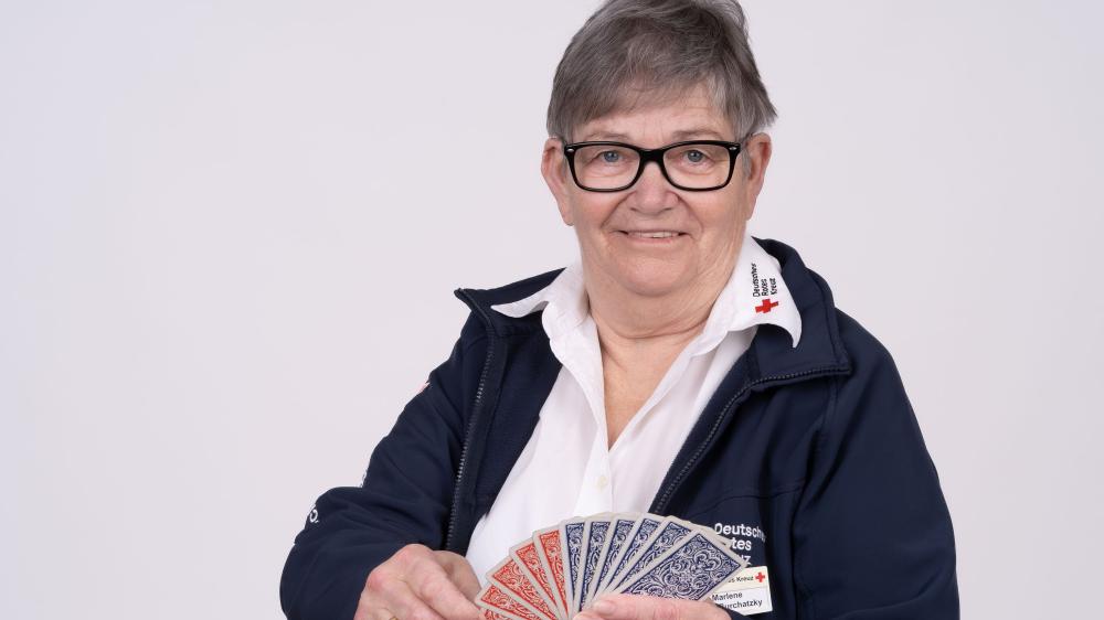 Frau vor weißem Hintergrund mit Spielkarten in der Hand.