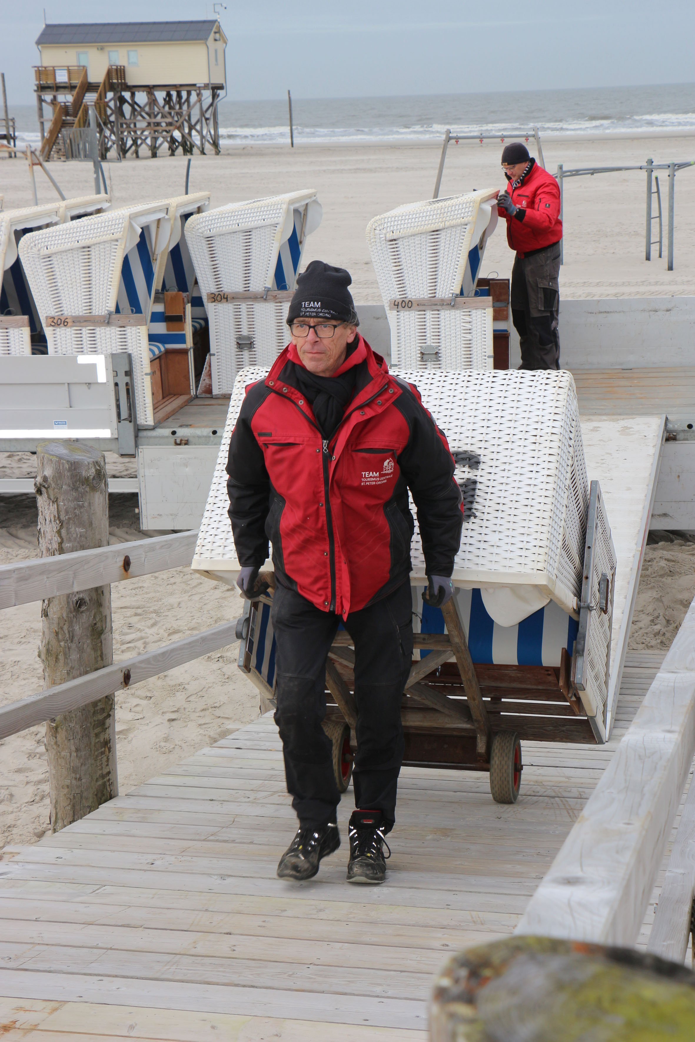 Mitarbeiter der Tourismus-Zentrale St. Peter-Ording stellen erste Strandkörbe auf die Podeste am Strand auf.