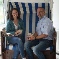 Eine Frau und ein Mann sitzen in einem Strandkorb. Sie halten Schokoladentafeln in der Hand.