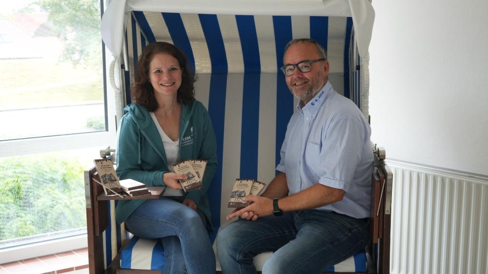 Eine Frau und ein Mann sitzen in einem Strandkorb. Sie halten Schokoladentafeln in der Hand.