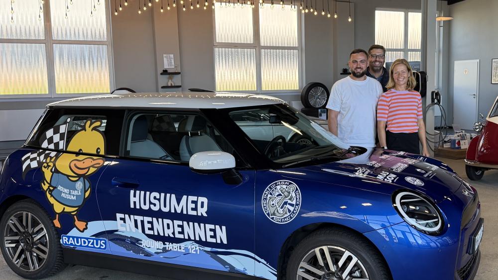 Menschen stehen im Autohaus hinter einem Auto der Firma Mini.