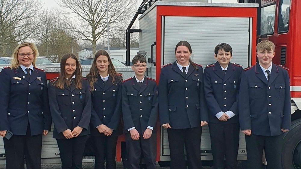 Jugendliche stehen vor einem Leiterwagen der Feuerwehr. Sie tragen blaue Feuerwehruniformen.