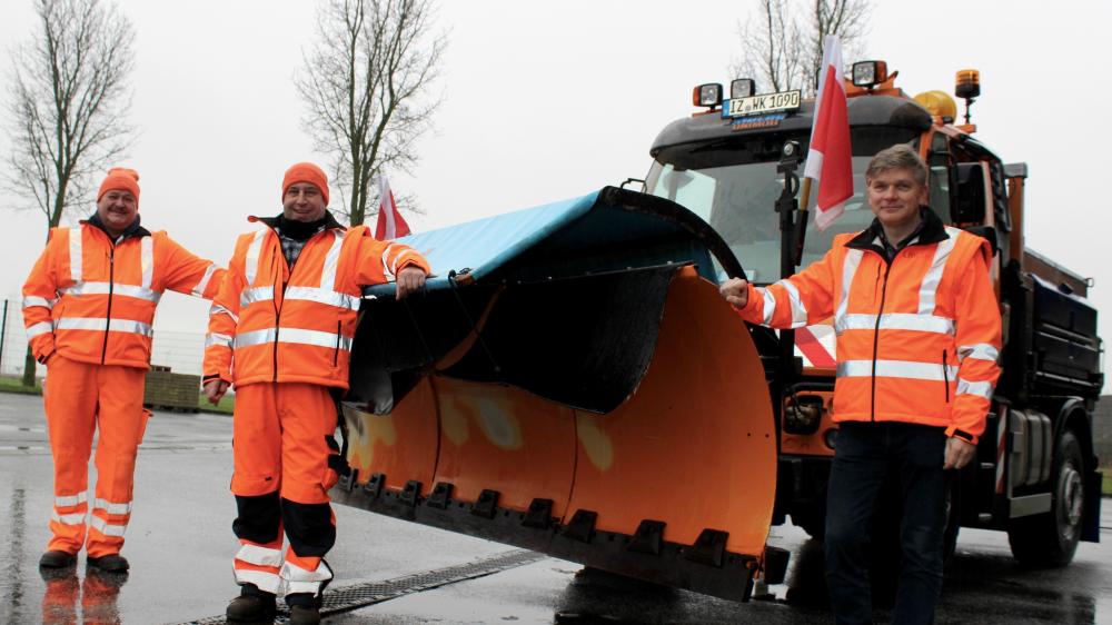 Männer in Orange vor einem ebenfalls orangenen Unimog.