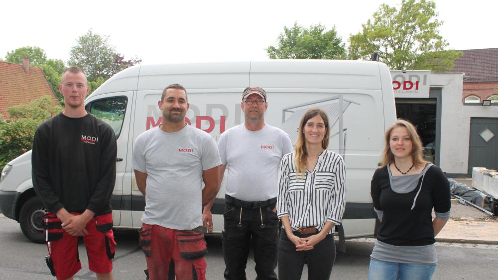 Drei Männer und zwei Frauen stehen in einem Hof vor einem Transporter, auf dem MODI steht.